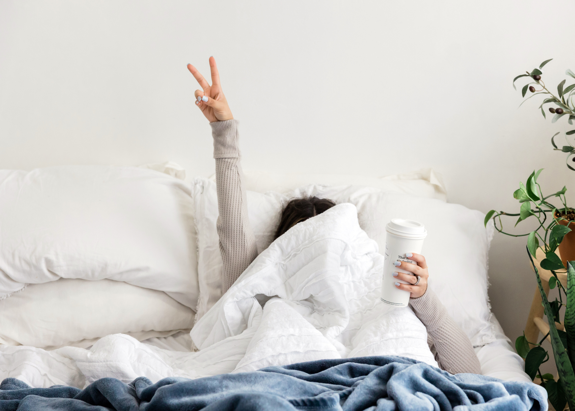 Person under covers in bed showing peace sign